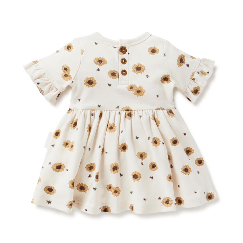 Back of sunflower dress for babies and kids, showing coconut buttons at the neckline, ruffle sleeves, full skirt, and bright yellow sunflowers on a cream background