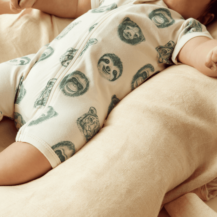 Baby in a Wilson & Frenchy Organic Boyleg Zipsuit with sloth print, lying on a cushion.