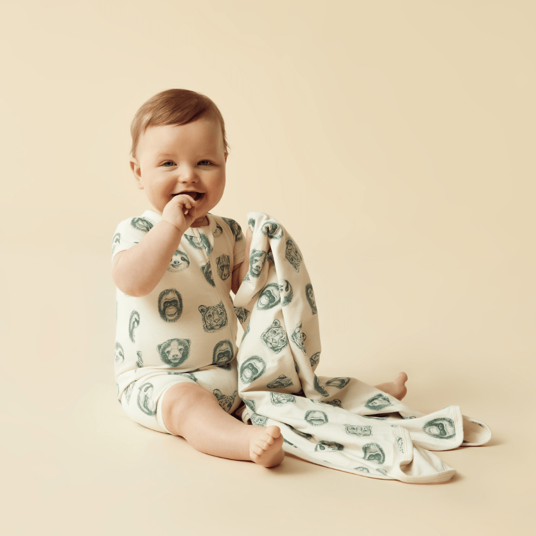 A smiling baby sitting with a Wilson & Frenchy Organic Boyleg Zipsuit on a beige background.