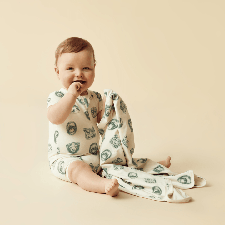 A Wilson & Frenchy Organic Baby Swaddle Blanket - LUCKY LAST - TROPICAL GARDEN ONLY baby sitting on the floor.