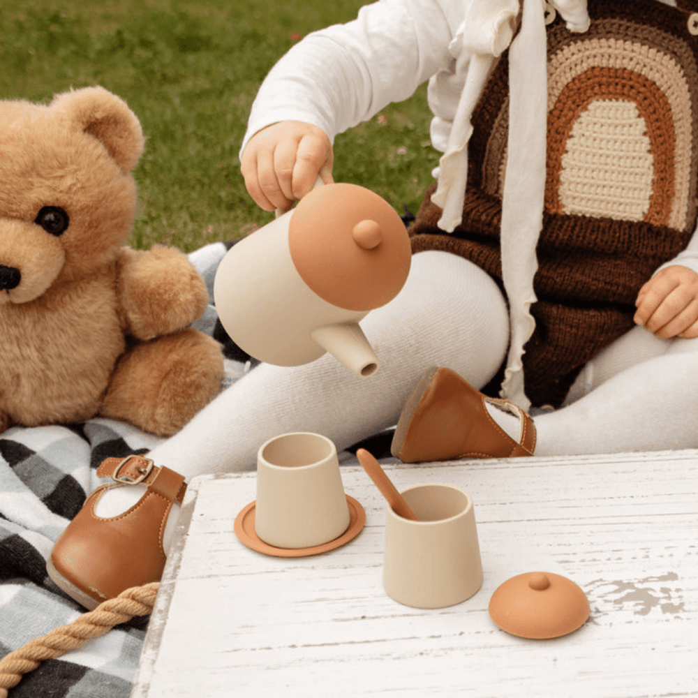 A little girl is playing with the Classical Child Silicone Tea Set and her teddy bear.