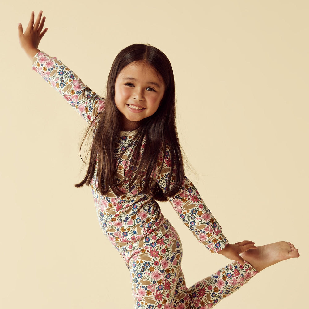 Young girl posing playfully in Wilson & Frenchy Organic Long Sleeve Easter Pyjamas with a floral outfit against a beige background.
