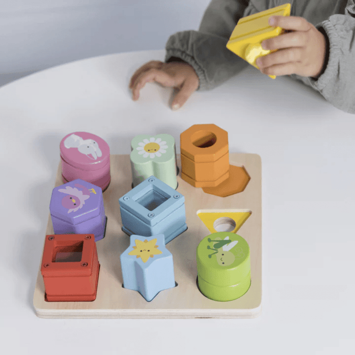 A child is engaged in play with a Le Toy Van Petilou Sensory Shapes, developing their fine motor skills and exploring sensory shapes on a table.