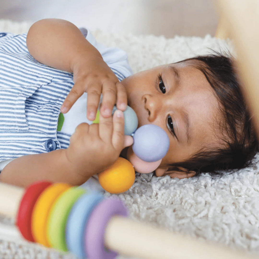 A baby is engaging in tactile exploration with the Le Toy Van Wooden Teething Beads toy.