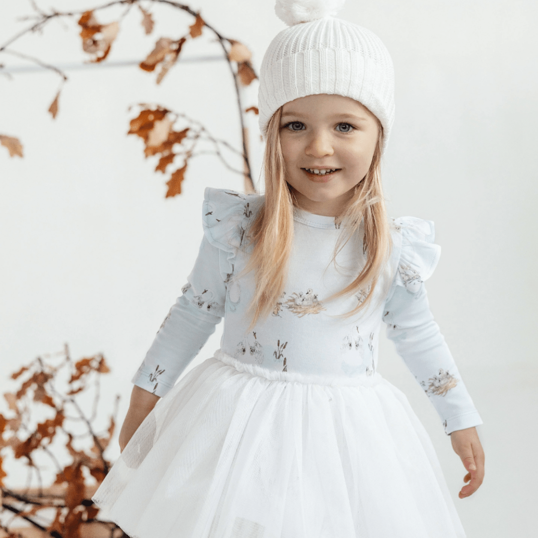 Close-up-of-Smiling-Little-Girl-Wearing-Aster-and-Oak-Organic-Cotton-Pom-Pom-Beanie-Snow-Naked-Baby-Eco-Boutique