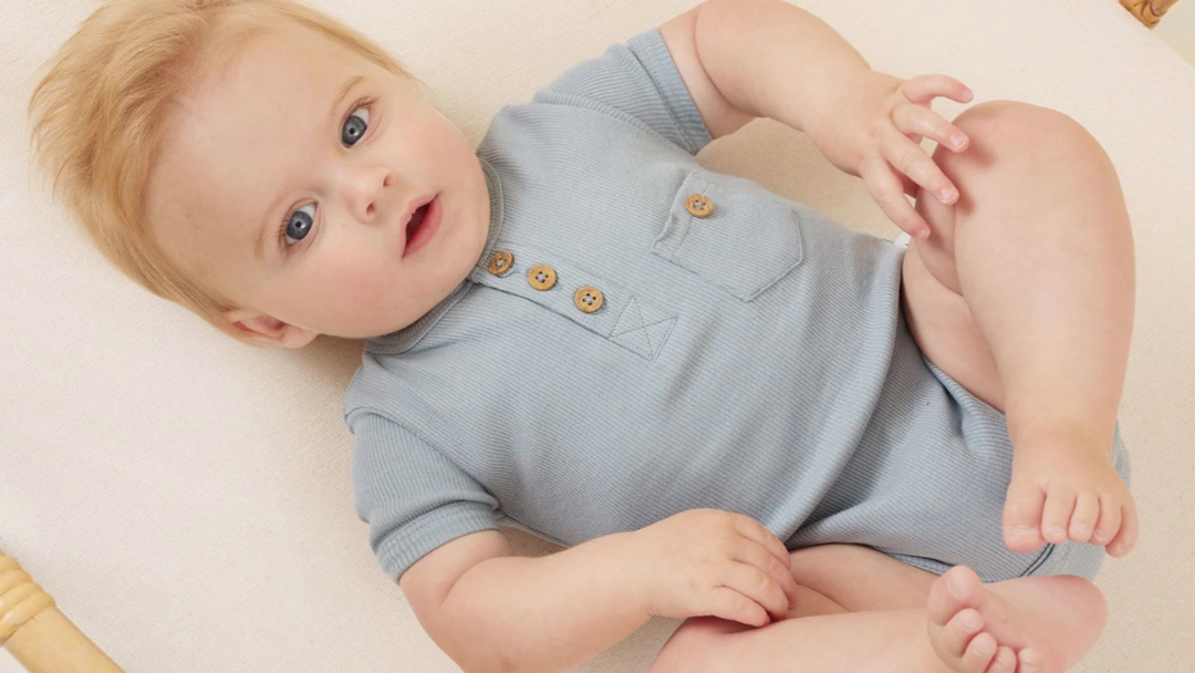 A baby is laying on a bed wearing a blue romper.