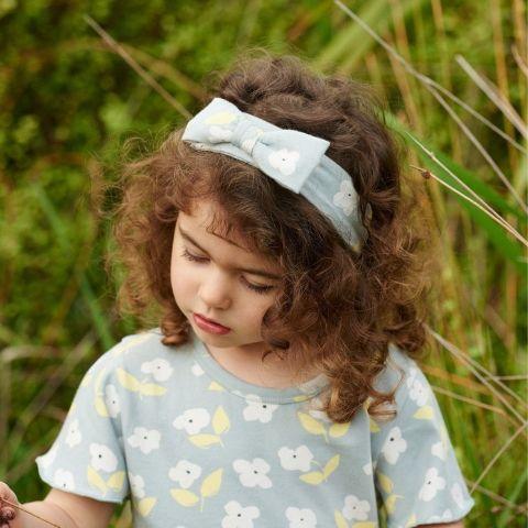 A little girl wearing a blue floral t - shirt and flower headband.