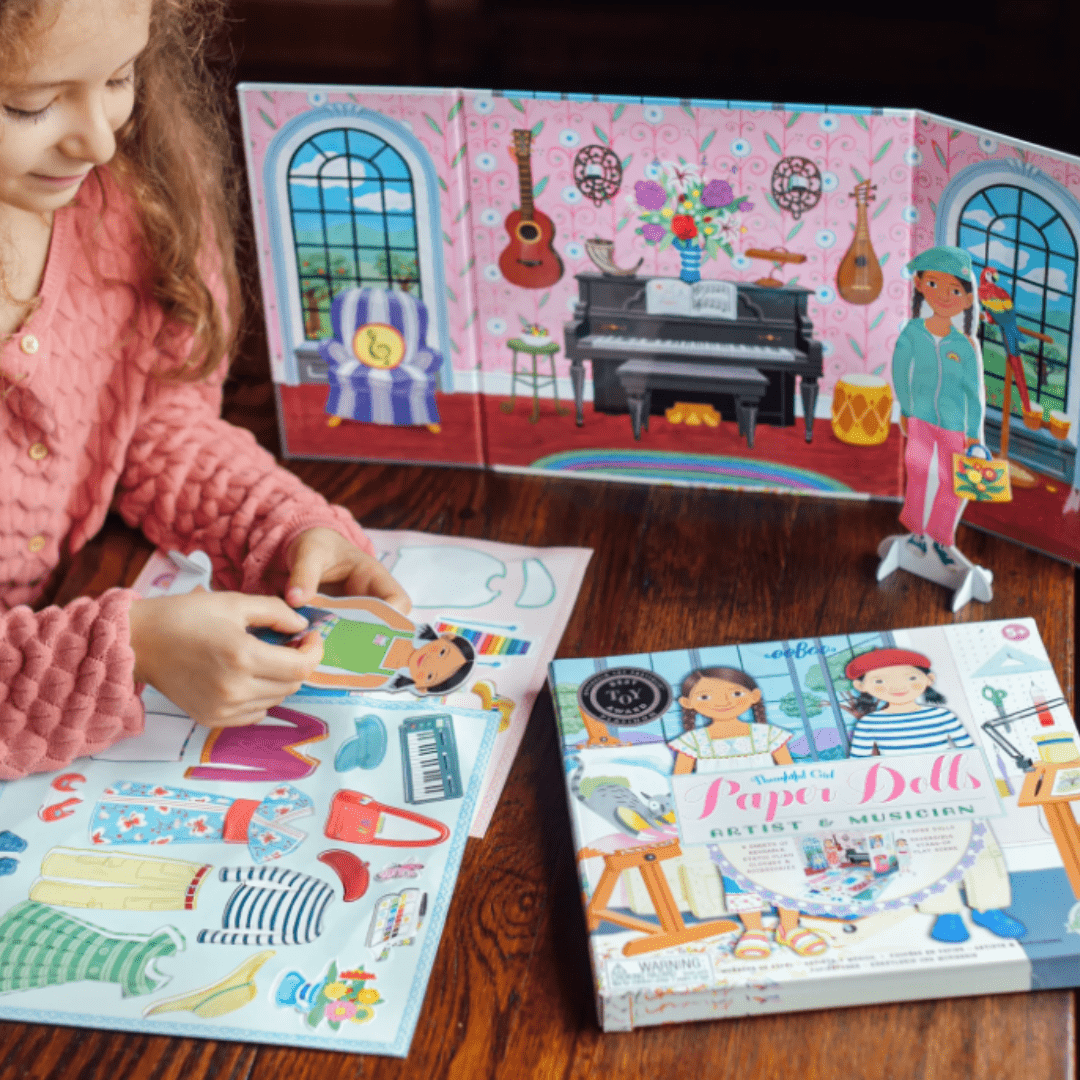 A little girl is playing with an eeBoo Paper Doll Set and book.