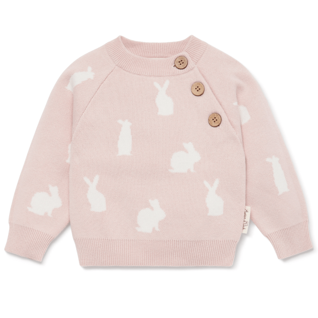 An Aster & Oak organic knit bunny jumper in pink for the baby winter style, featuring a pattern of white rabbits and wooden buttons on the shoulder.