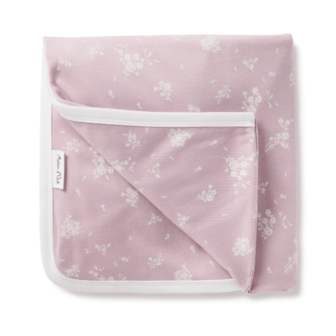 An Aster & Oak Organic Cotton Baby Swaddle Wrap with a hand-illustrated print of pink blanket with white flowers on it.