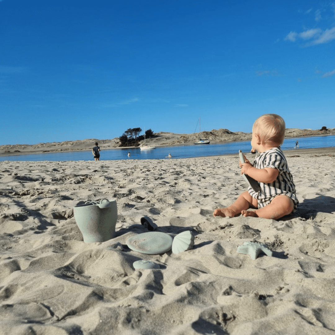 A baby playing with Classical Child Silicone Beach Bucket Set With Frisbee in the sand on a beach.