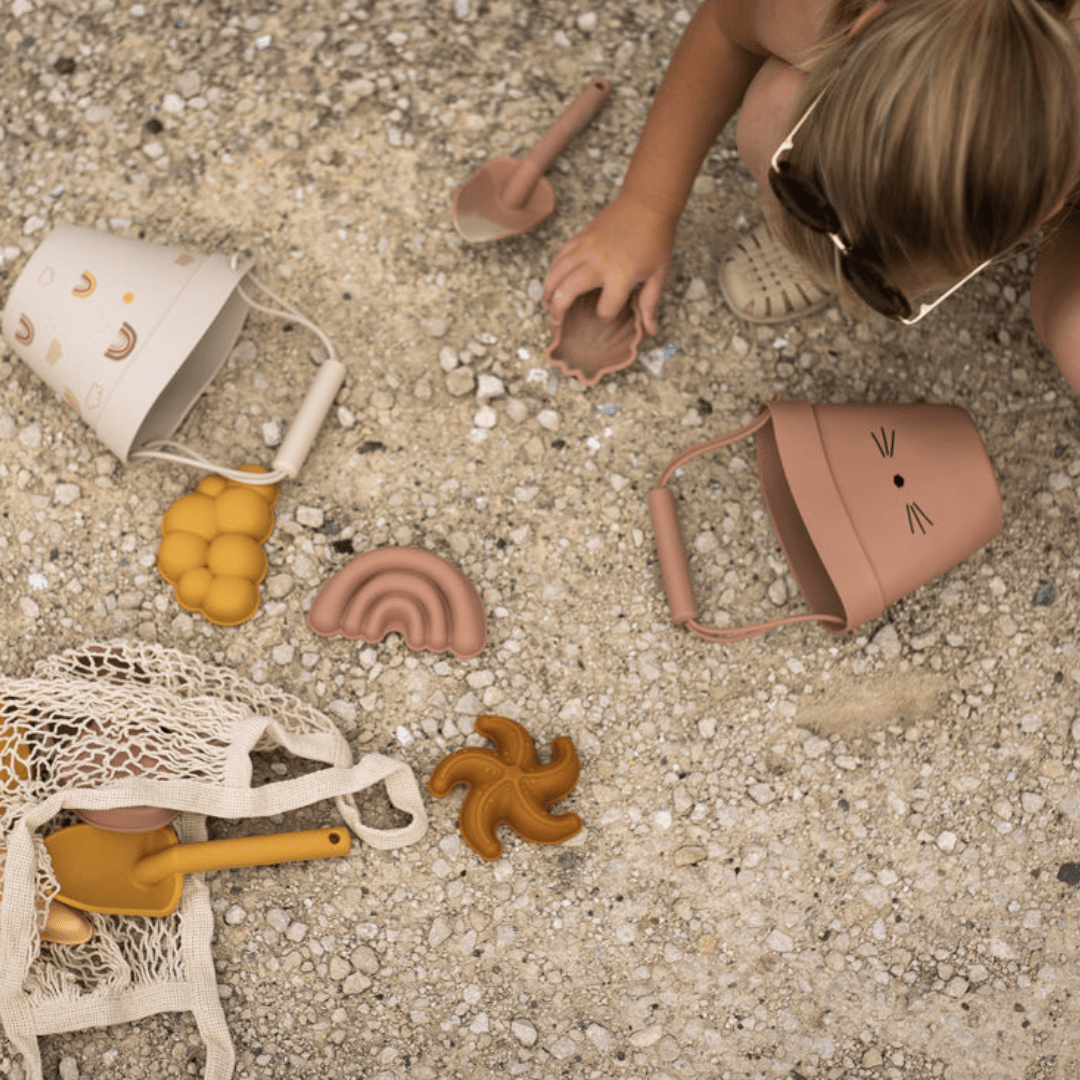 A little girl is playing with the Classical Child Silicone Sand Set beach toys on the ground.