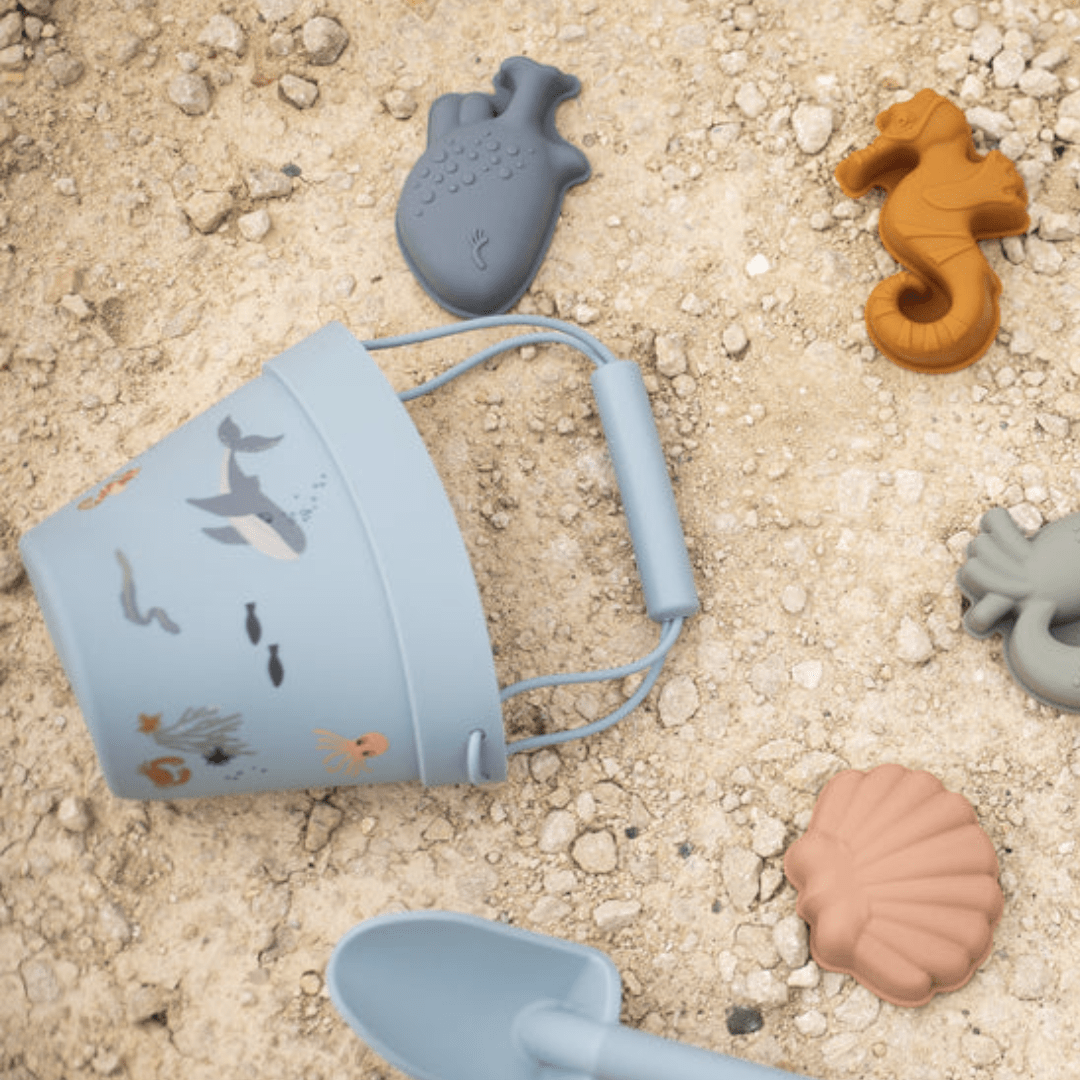 An eco-friendly blue bucket with Classical Child Silicone Sand Sets, featuring sea animals and a shovel, resting on the sand.