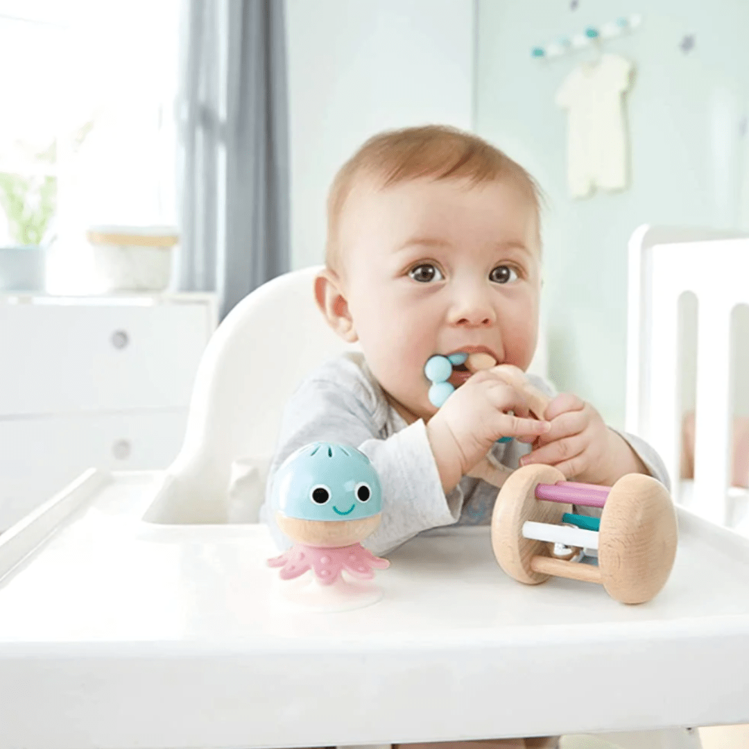 A baby is sitting in a high chair playing with a Hape Baby To Toddler Sensory Gift Set.
