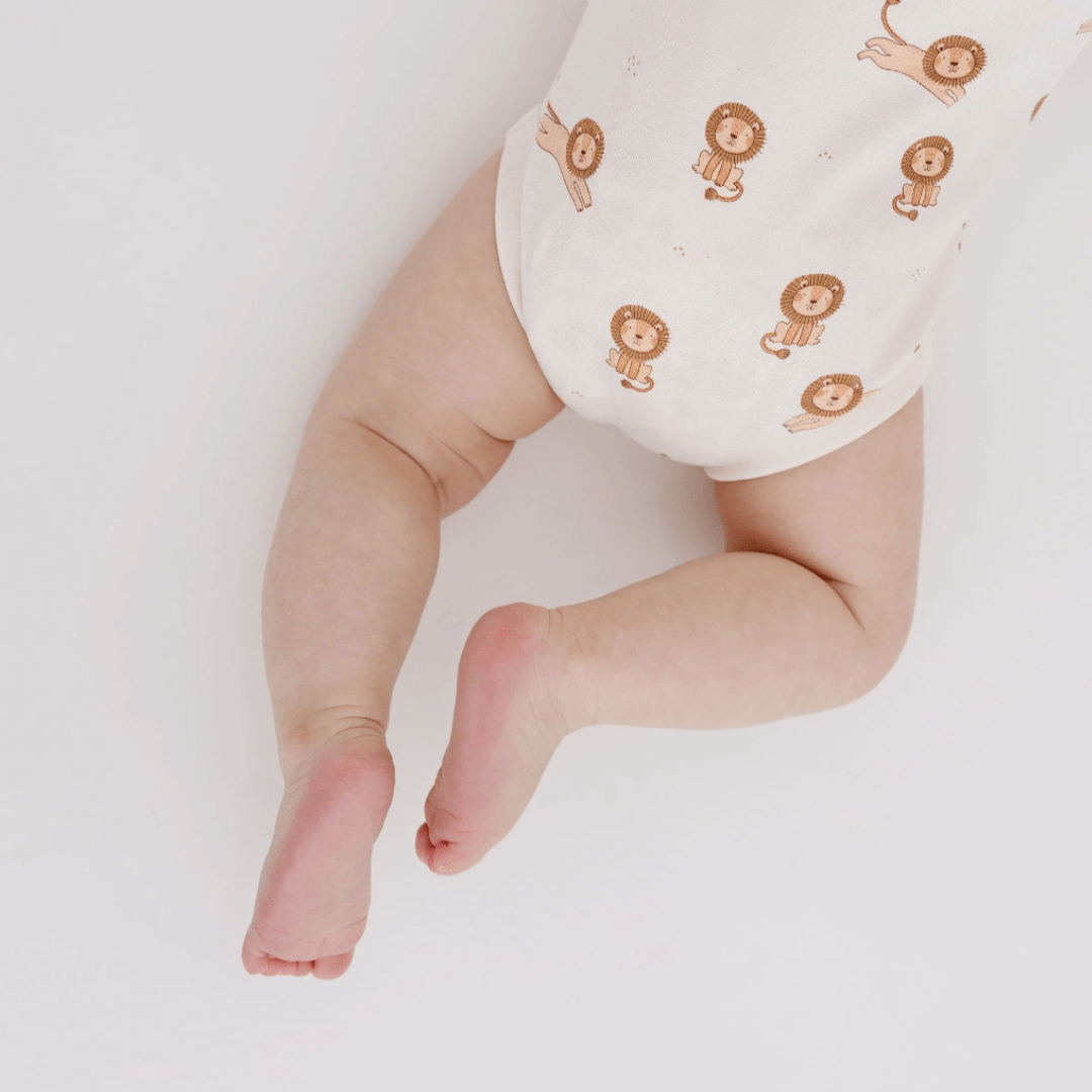 A baby's legs in an Aster & Oak Organic Cotton AOP Henley Onesie with a lion pattern against a white background.