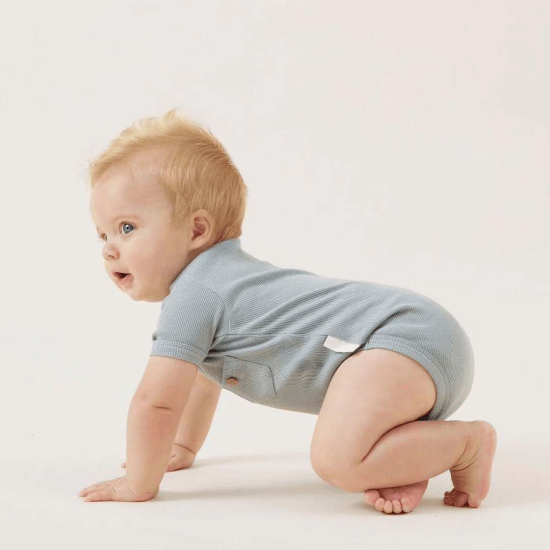 A baby on hands and knees wearing an Aster & Oak Organic Rib Henley Onesie in Lucky Lasts color, made of organic cotton against a white background.