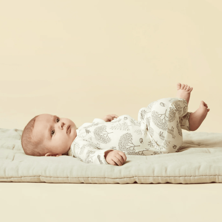 Baby lying on a soft surface against a plain background, dressed in Wilson & Frenchy Organic Baby Pyjamas with leaf pattern.
