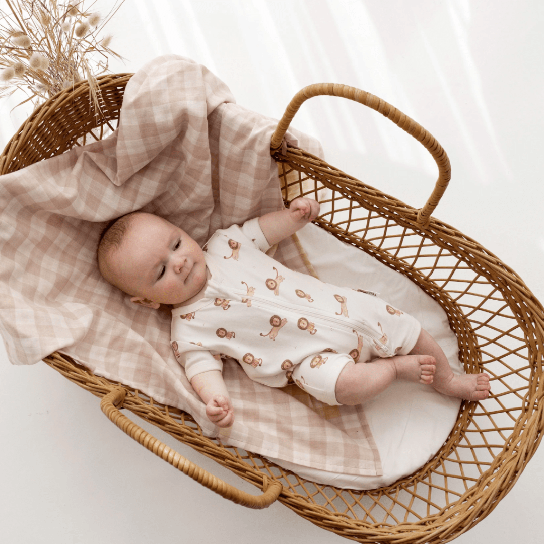 A baby laying in a wicker basket with an Aster & Oak Organic Cotton Zip Romper.
