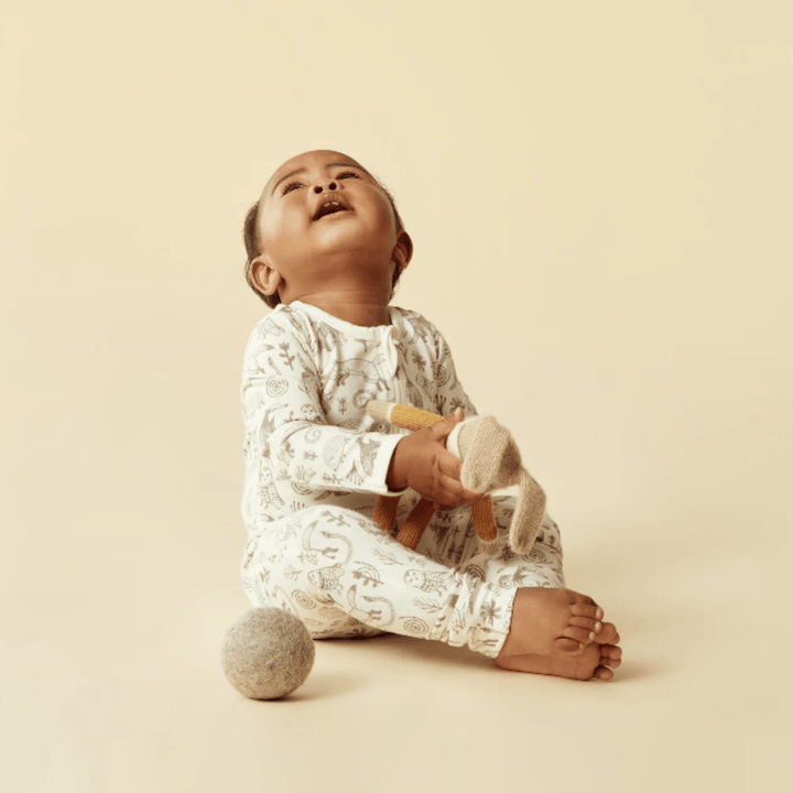 Infant sitting and looking upwards in Wilson & Frenchy Organic Baby Pyjamas, featuring a hand-illustrated print, against a neutral background.
