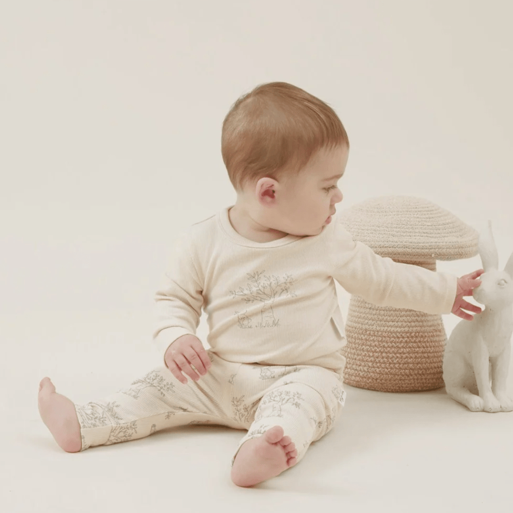 Baby sitting and reaching out towards a white rabbit figurine, wearing Aster & Oak Organic Bunny Luxe Rib Leggings.