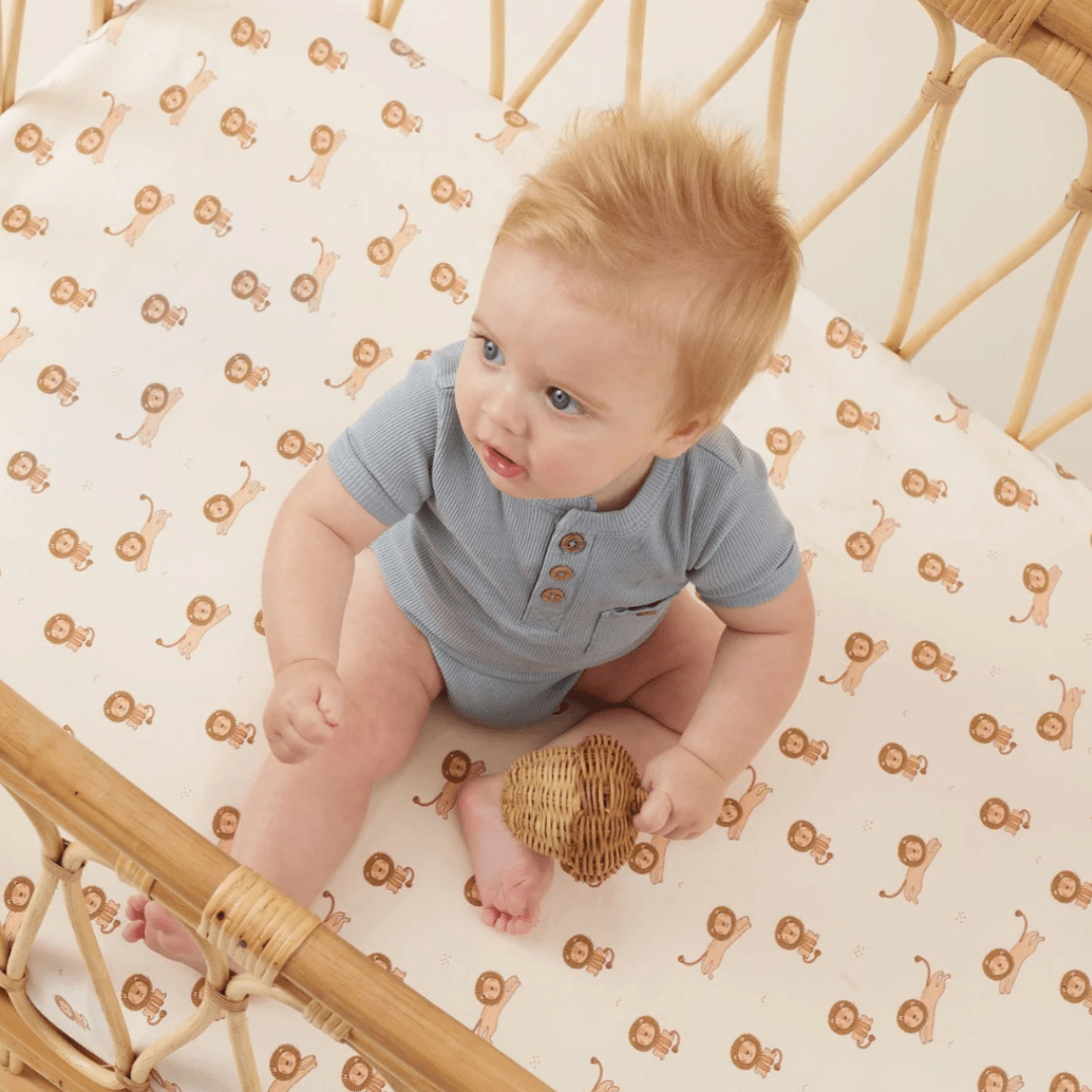 Baby sitting in a crib with an Aster & Oak Organic Rib Henley Onesie surrounded by a monkey-patterned mattress.