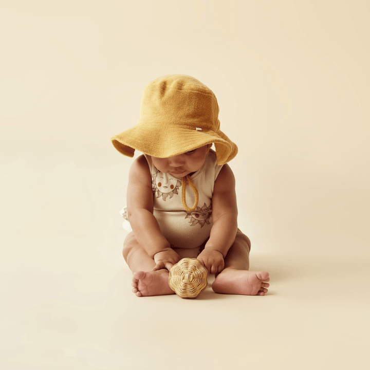 A baby in a Wilson & Frenchy Organic Terry Sunhat, playing with a ball by Wilson & Frenchy.