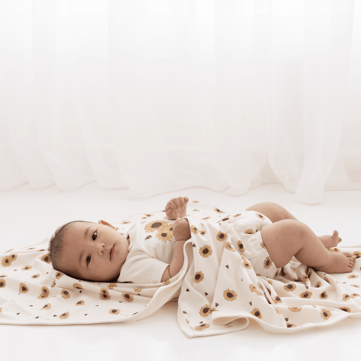 An Aster & Oak Organic Cotton Baby Swaddle Wrap adorned with hand-illustrated sunflower print.