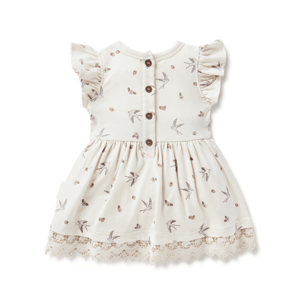 Back view of off-white dress for babies and kids, featuring a hand-illustrated swallow and strawberry print, four coconut buttons, ruffle sleeves, and full skirt trimmed with delicate lace
