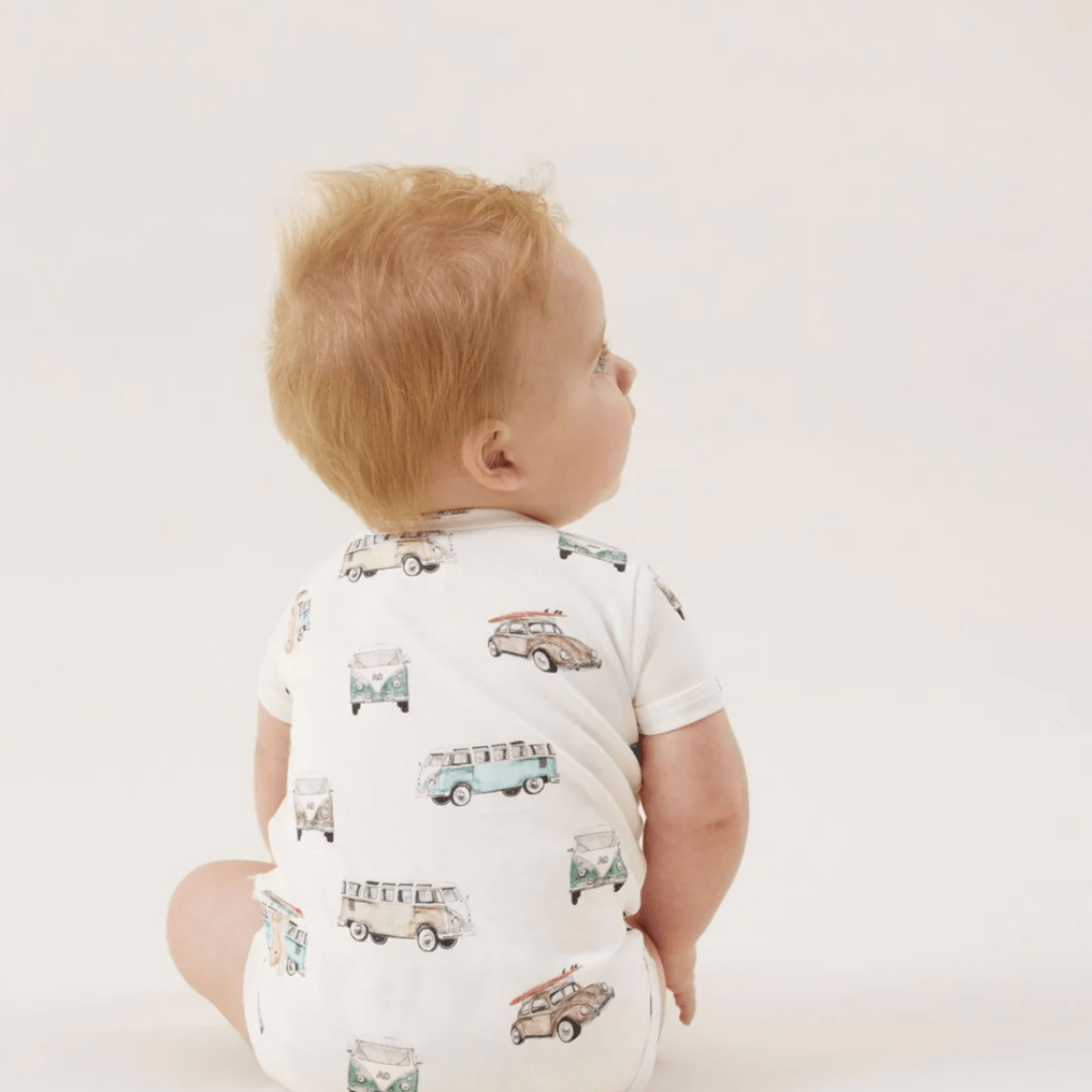 Baby sitting and looking to the side, wearing an Aster & Oak Organic Cotton AOP Henley Onesie with Lion print.