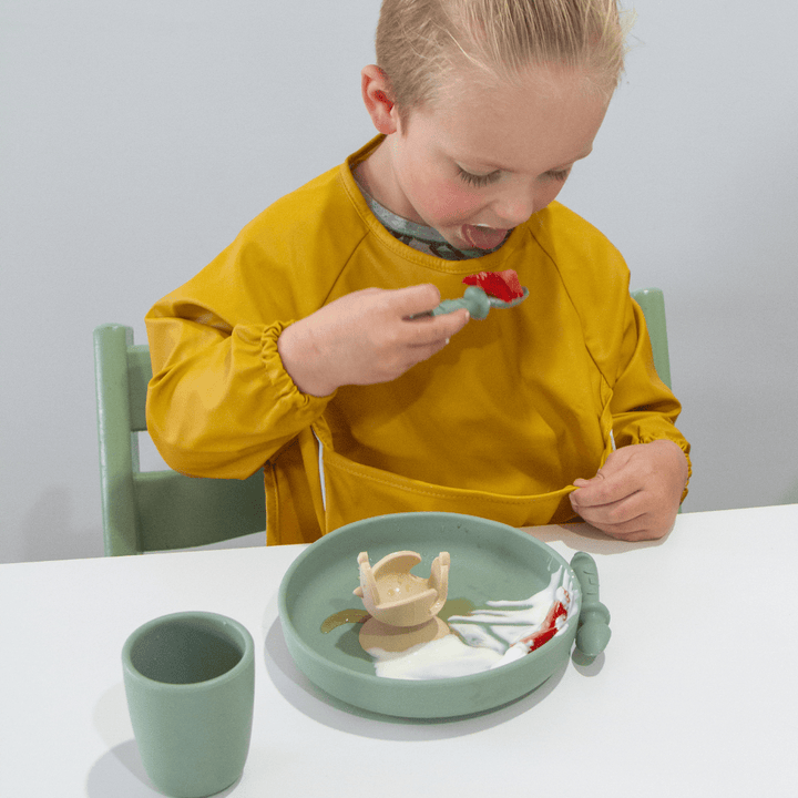 A young boy wearing a Zazi Recycled Full-Sleeved Bib (Multiple Variants) eating from a plate.