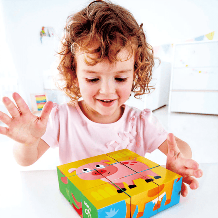 A little girl is playing with a Hape Animal Block Puzzle (Multiple Variants) featuring Farm Animals and Jungle Animals.