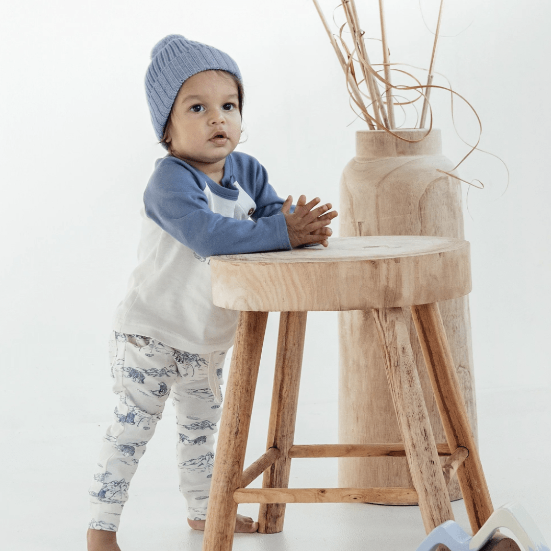 Child-Leaning-on-Stool-Wearing-Aster-and-Oak-Organic-Cotton-PomPom-Beanie-Navy-Naked-Baby-Eco-Boutique