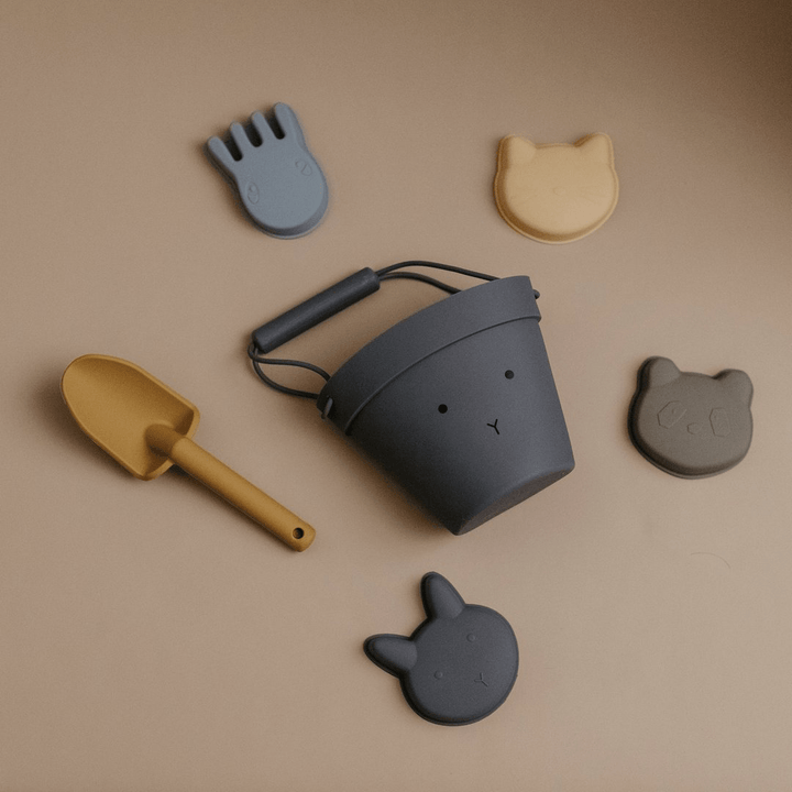 An eco-friendly Classical Child Silicone Sand Set, consisting of a bucket, shovel, and cat and dog toys, arranged on a beige surface.