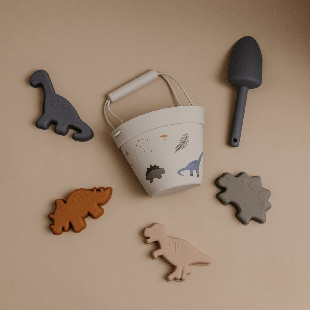 An eco-friendly Classical Child Silicone Sand Set featuring a bucket filled with dinosaurs and a shovel, set against a soothing beige background. Perfect beach toys for endless hours of imaginative play.