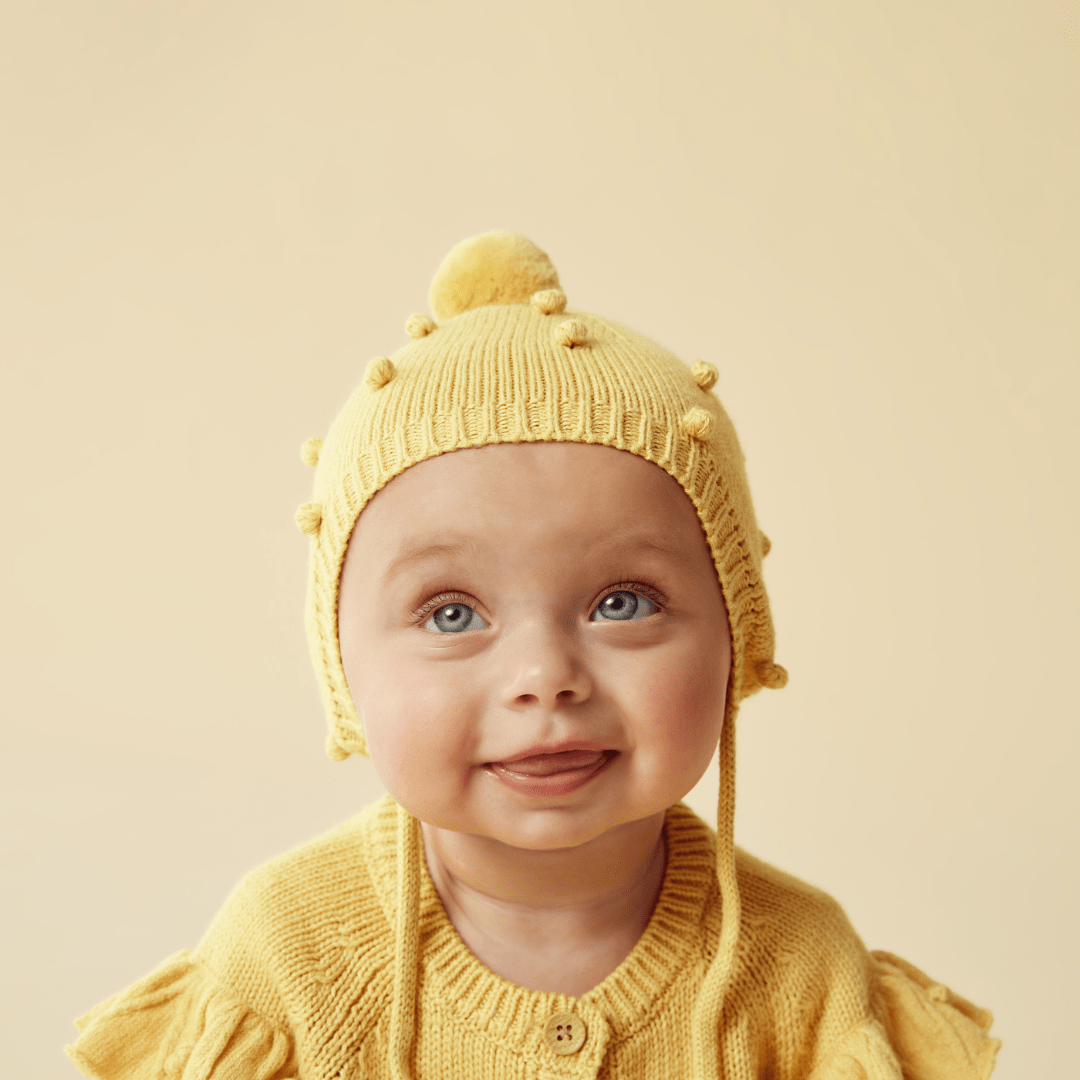 Close-Up-Of-Happy-Baby-Wearing-Wilson-And-Frenchy-Knitted-Bauble-Bonnet-Dijon-Naked-Baby-Eco-Boutique