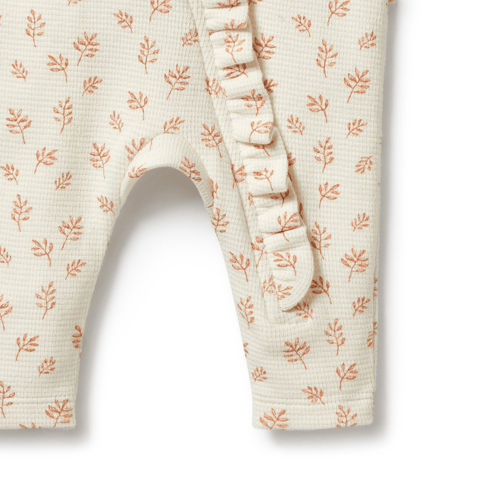 Close-up of a Wilson & Frenchy Organic Waffle Ruffle Zipsuit with a coral pattern on a cream background.
