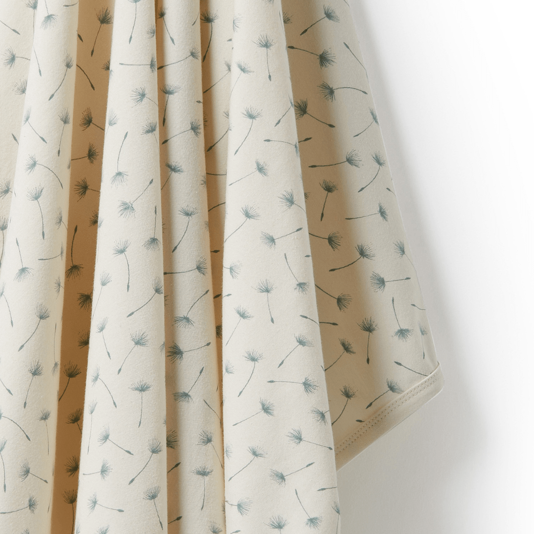 A Wilson & Frenchy luxury baby swaddle blanket with dandelions on organic fabric.