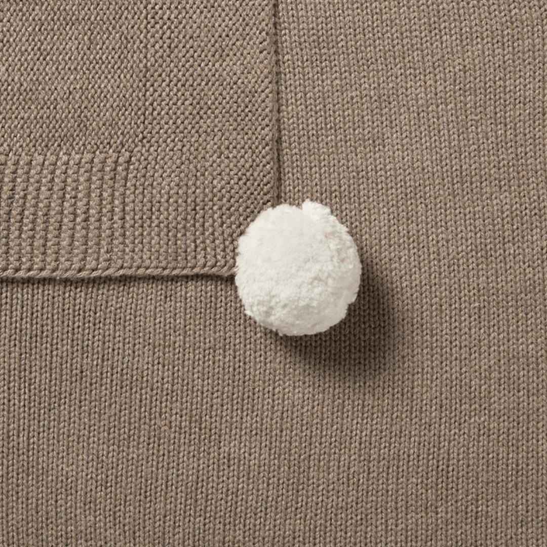 A white pompom attached to a Wilson & Frenchy Knitted Baby Blanket.