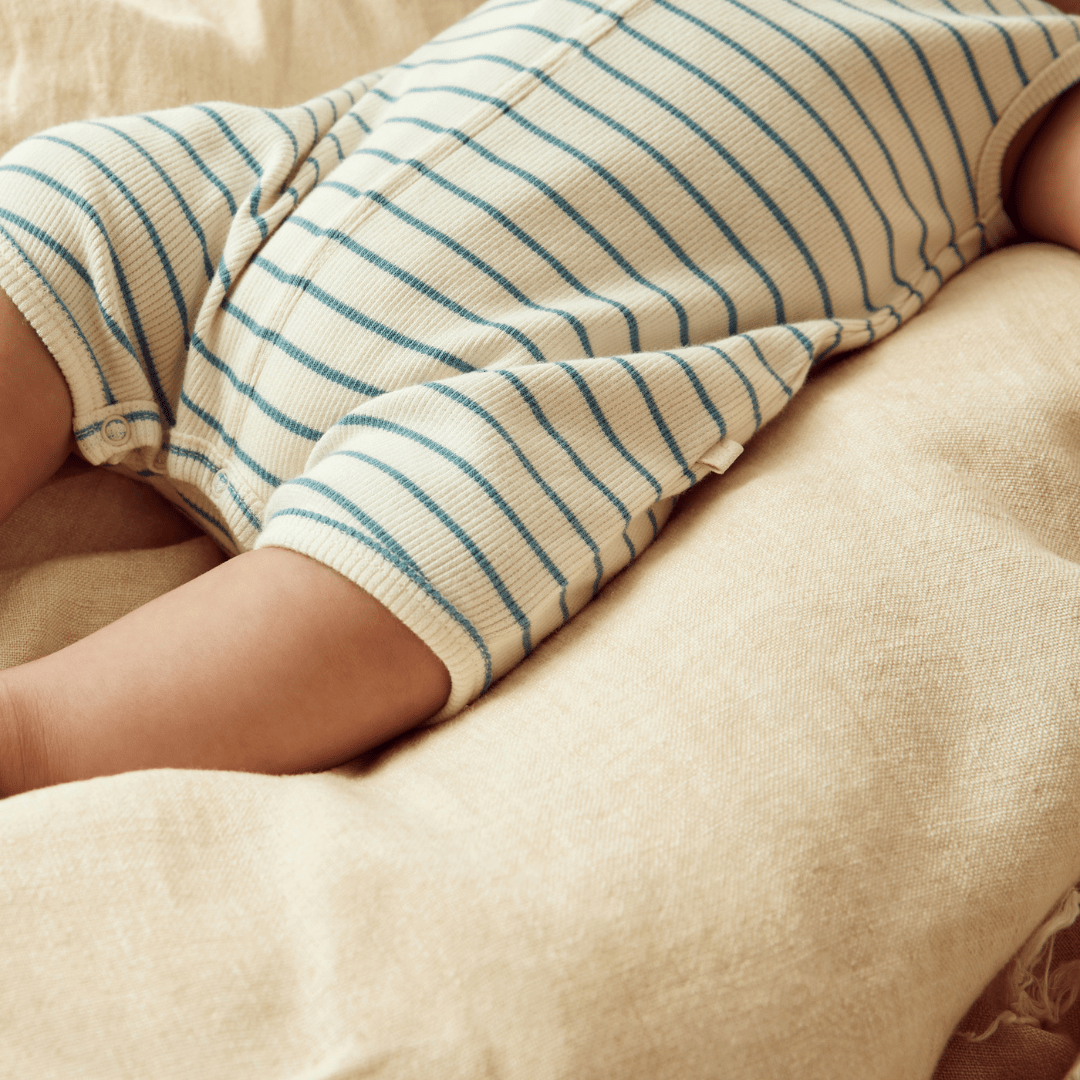 A baby in a Wilson & Frenchy Organic Rib Stripe Henley Growsuit laying on a bed.