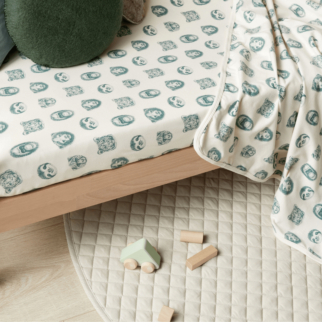 A bed with the Wilson & Frenchy Organic Cotton Cot Sheet - LUCKY LASTS - FLOAT AWAY ONLY blanket and toy blocks on the floor.