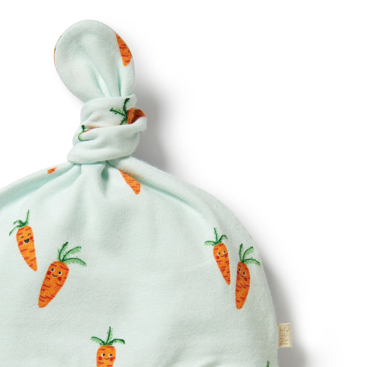 A Wilson & Frenchy Organic Easter Knot Hat made of organic cotton, featuring an adjustable knot on top, with a carrot print on a pale green background.
