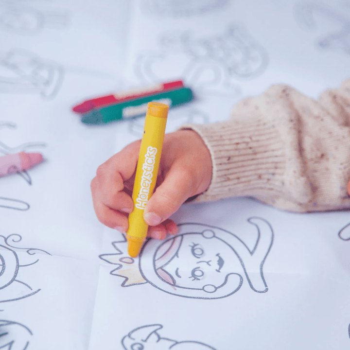 A child is unleashing their creativity by using Honeysticks pure beeswax crayons to draw on a coloring sheet from the Honeysticks Jumbo Poster & Crayon Activity Set.