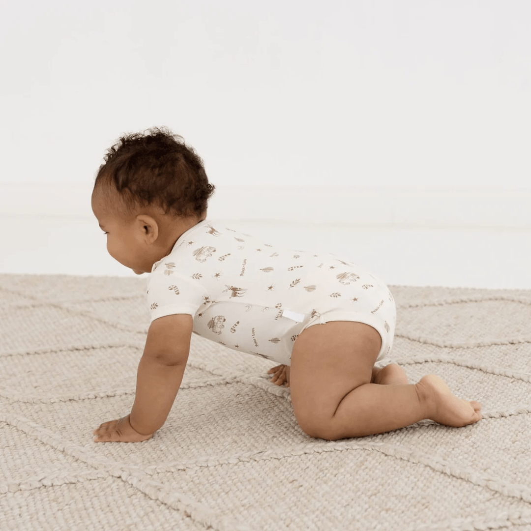 A baby crawling on a rug in an Aster & Oak Organic Happy Holidays onesie.