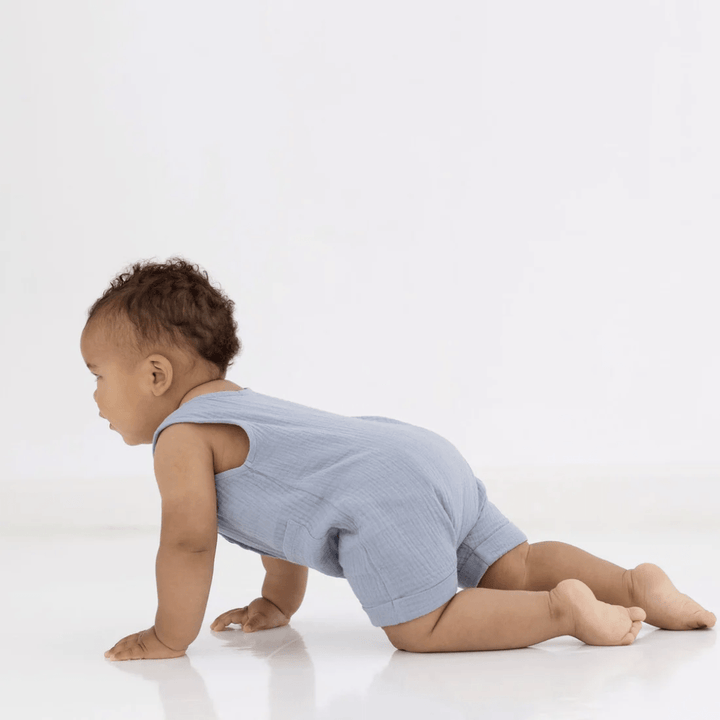 A baby crawling on the floor in an Aster & Oak Organic Slate Blue Muslin Romper for the summer.