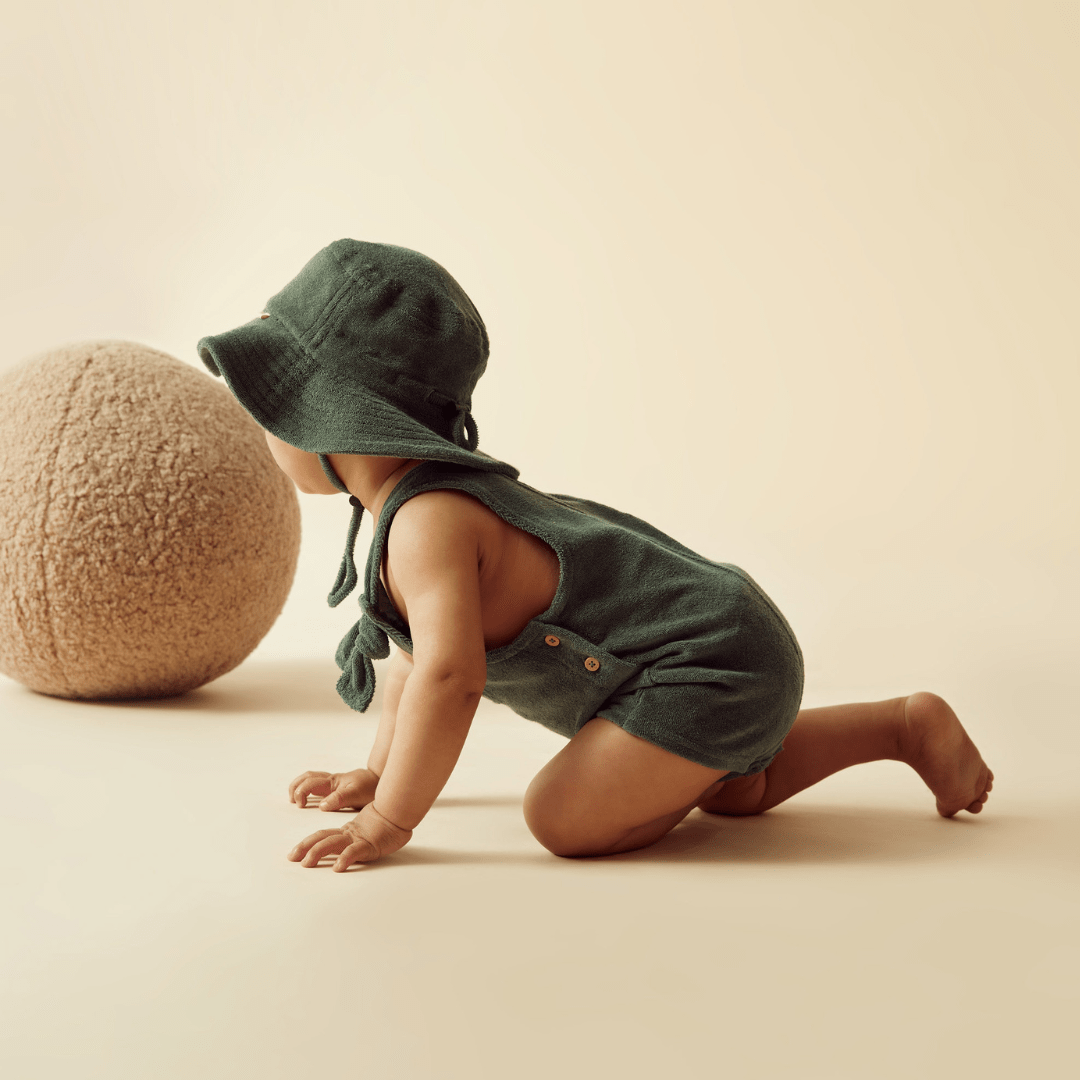 A baby in a green romper and Wilson & Frenchy Organic Terry Sunhat- LUCKY LAST - SUN DIAL - 6-12 MONTHS.