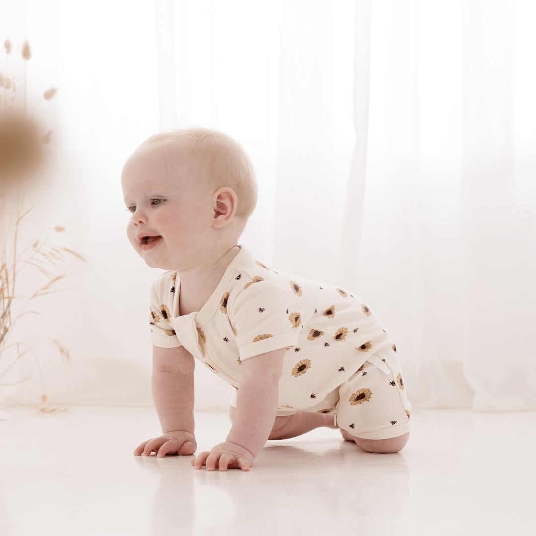 A baby crawling on the floor in an Aster & Oak Organic Cotton Zip Romper.