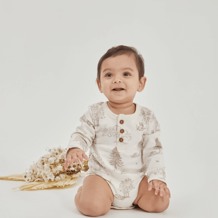 A baby in an Aster & Oak Organic Henley Long-Sleeved Onesie sitting with dried flowers on a white background.