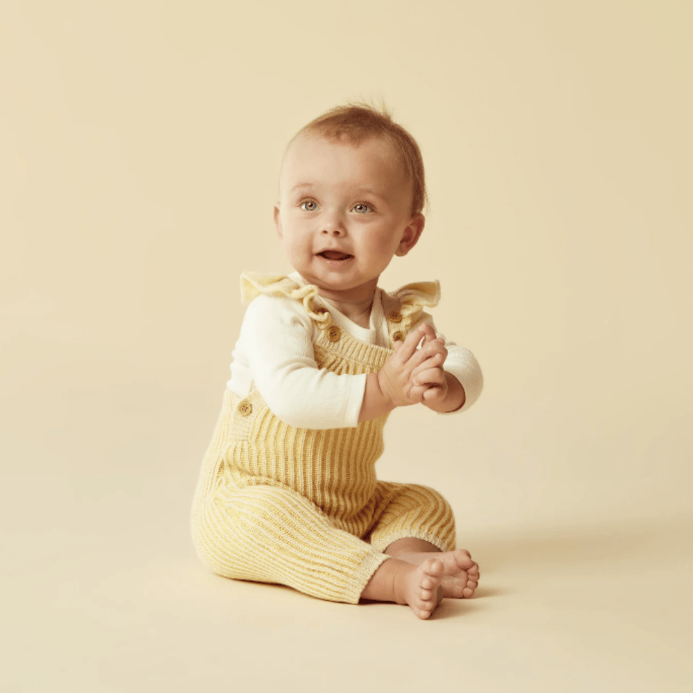 A baby in Wilson & Frenchy Knitted Ruffle Overalls sitting against a light background.