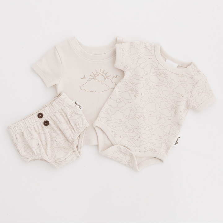 Cream Coloured Baby Bloomers, Baby Onesie, and Baby T-Shirt With Sun and Cloud Illustration On Them Lying Flat On A White Background