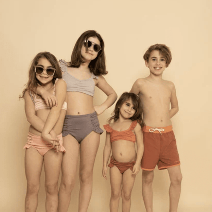 A group of children in swimsuits, including Grech & Co. UPF 40+ Recycled Swim Trunks, posing for a picture.